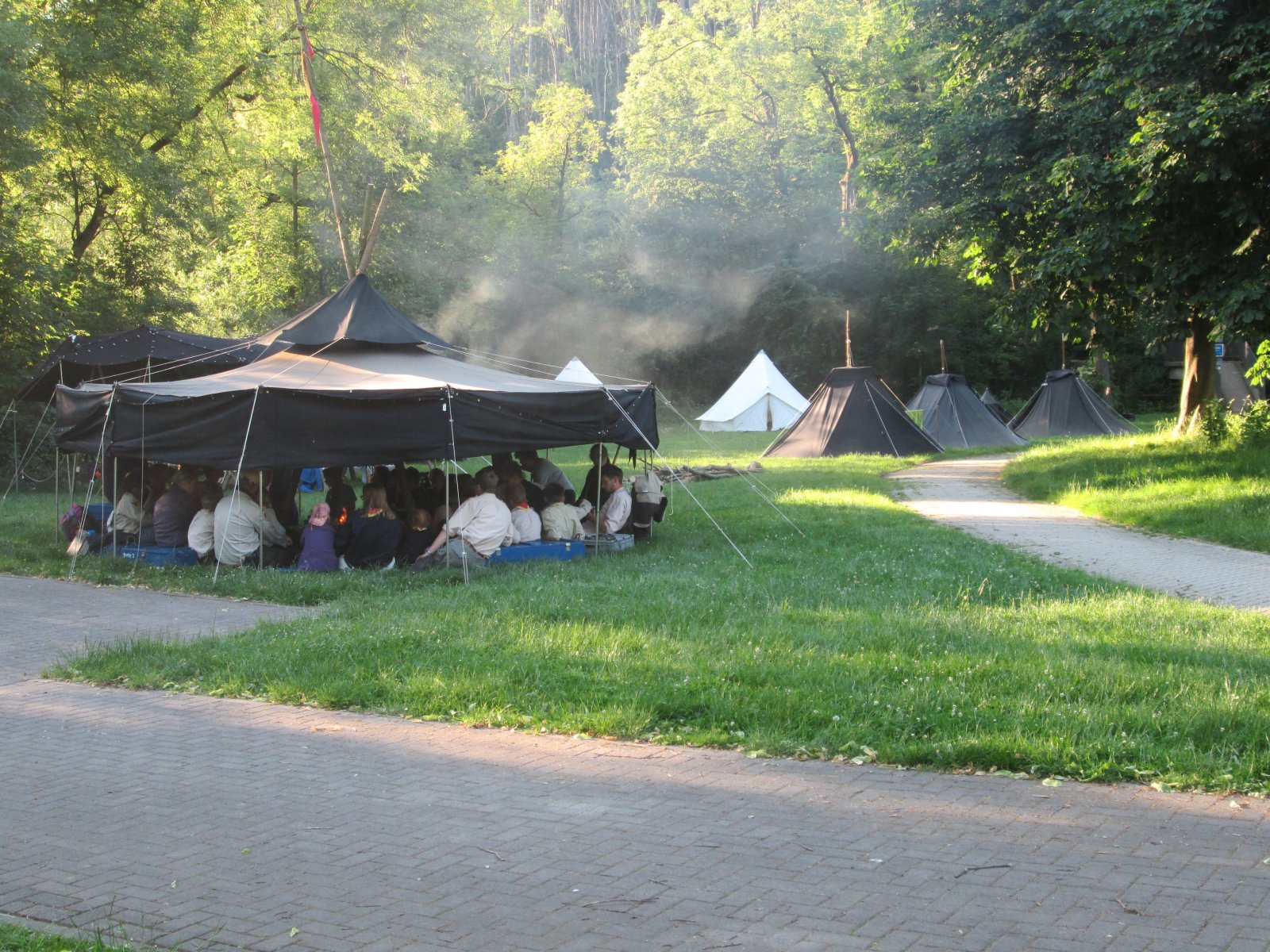 Ein Foto des Lagerplatzes des Stammeslagers 2019 in Etteln. Es sind eine Jurte (großes, rundes, schwarzes Zelt), drei Kothen (kleinere, schwarze Zelte) und zwei Igel (weiß und etwas größer als Kothe) zu sehen.