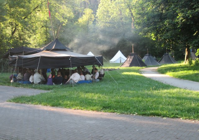 Ein Foto des Lagerplatzes des Stammeslagers 2019 in Etteln. Es sind eine Jurte (großes, rundes, schwarzes Zelt), drei Kothen (kleinere, schwarze Zelte) und zwei Igel (weiß und etwas größer als Kothe) zu sehen.